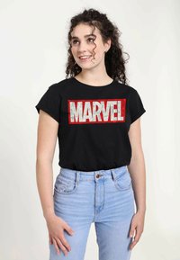 Camiseta negra de manga corta con un gran logotipo en rojo y blanco de "MARVEL". Diseño de cuello redondo, combinada con unos vaqueros de tiro alto en azul claro.
