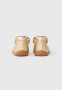 Goldfarbene, texturierte Leder-Stiefeletten mit einer weichen, braunen Gummisohle und einem Klettverschluss am Knöchel, designed für Komfort und einfachen Tragekomfort.