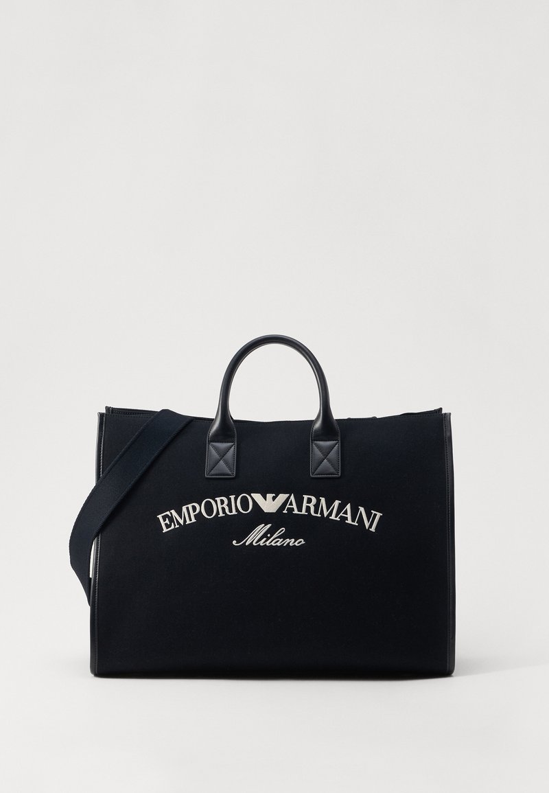Black canvas tote bag with leather accents, featuring the embroidered "Emporio Armani Milano" logo in silver. Double handles and detachable strap.