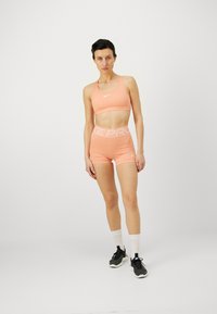Porsjonert treningstopp og shorts-sett i ferskenfarge med hvit "NIKE PRO" midjebånd; har fukttransporterende stoff og en strømlinjeformet passform.