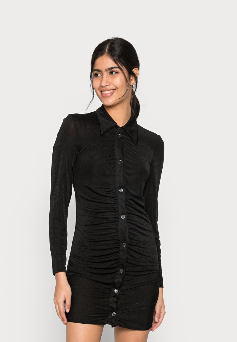 Vestido preto com franzido, mangas longas, colarinho e fecho frontal em botão. Tecido suave e texturizado com uma silhueta ajustada.