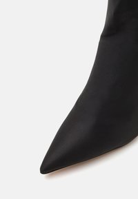 Zapato negro de punta afilada, hecho de satén suave, con una silueta elegante y delgada y un diseño minimalista.