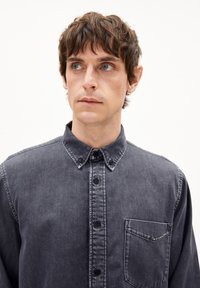 Dunkelgraues Jeanshemd mit verbreiteter Kragen, Knopfleiste vorne und einer linken Brusttasche. Hat eine weiche Textur und ein lässiges Design.
