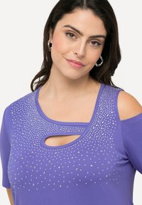 Paarse top met korte mouwen en een cold shoulder ontwerp, versierd met zilveren rhinestones in een gradient patroon, met een keyhole halslijn.