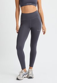 Dunkelgraue Sportleggings mit hohem Bund, glatter Textur und sichtbaren Nähten; Logo auf dem linken Wadenbereich gedruckt.