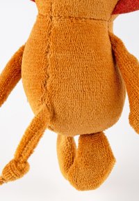 Textured orange plush toy with a rounded body, short limbs, and a red fabric accent on the head. Surface appears soft and fuzzy.
