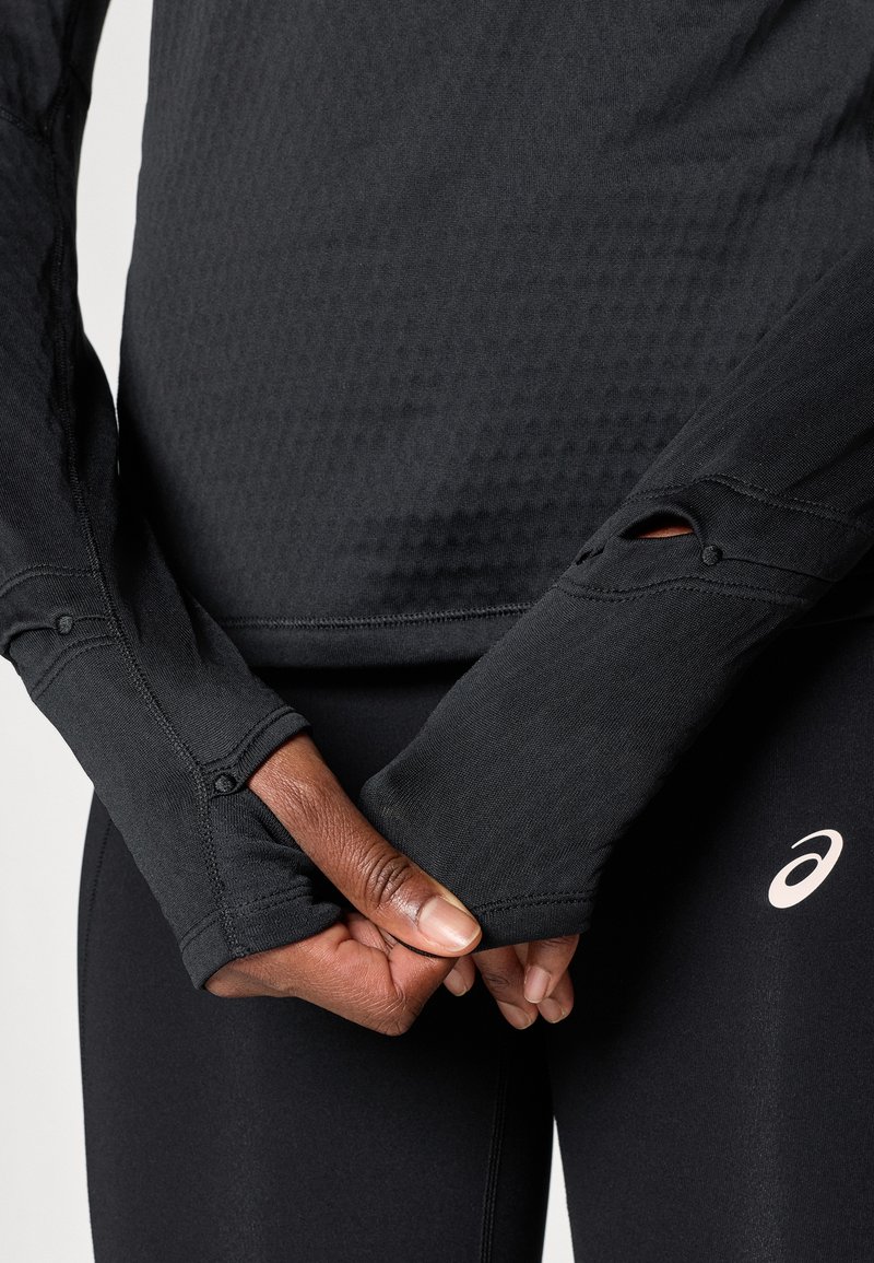 Zwarte sportieve top met lange mouwen van textuurstof, duimopeningen bij de manchetten en stikseldetails. Draag je met zwarte leggings met logo.