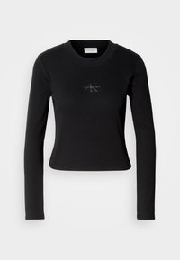 Crna majica dugih rukava s uskim dizajnom i malim Calvin Klein logom na prsima, prikazana na bijeloj pozadini.