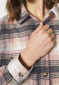 Plaid flannel shirt in pink, gray, and cream. Features button cuffs and a collar. Texture appears soft and warm.
