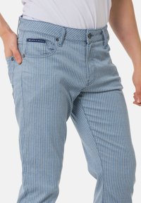 Hellblaue, gestreifte Jeans aus Denim mit klassischem Fünf-Taschen-Design, kontrastierenden Nähten und einem kleinen Markenetikett am Bund.