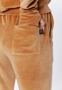 Beżowe skórzane dresy z wyraźną kieszenią po boku i widoczną metką, charakteryzujące się miękką, teksturowaną powierzchnią.