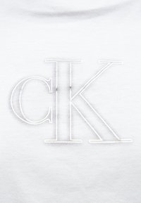 Tricou alb cu logo-ul "CK" brodat cu fir argintiu. Textură netedă a țesăturii, cu un design clasic cu gât rotund.