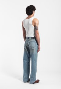 Losse lichtblauwe spijkerbroek van denim met een vervaagde textuur, gedragen met een wit tanktop. De jeans hebben een achterpatch label en een vijf-pocket ontwerp.