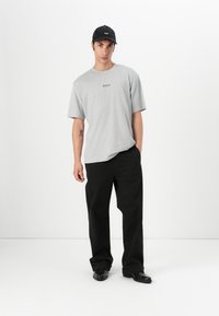 Tricou gri din bumbac, cu croială confortabilă, mâneci scurte și un logo subtil "BOSS". Asortat cu pantaloni negri, cu croială largă, și pantofi negri.