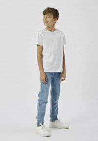 Tricou alb din bumbac cu mâneci scurte, combinat cu blugi din denim bleu deschis. Ținuta este completată de adidași sport albi.