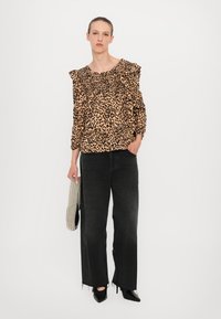 Dierprintblouse met ruches, effen zwarte wijde jeans, zwarte puntige hakken en een handtas van kralen. Neutrale achtergrond.