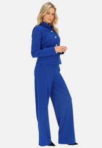 Niebieski dopasowany garnitur z taliowanym żakietem z złotymi guzikami i spodniami o szerokich nogawkach, wykonany z gładkiego materiału o eleganckim wykończeniu.