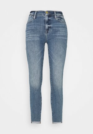 Jean skinny en denim bleu délavé, avec une taille haute, un design à cinq poches et une fermeture éclair avec un bouton doré.