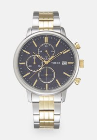 Timex chronografas su juodu tekstūruotu ciferblatu, sidabro ir auksinės spalvos nerūdijančio plieno korpusu bei dviejų tonų metaliniu dėklu.