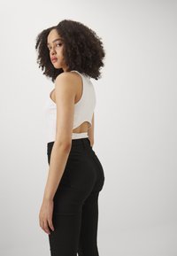 Fehér ujjatlan felső hátsó kivágással, magas derekú fekete nadrággal párosítva. Simább anyag, testhezálló fazon és minimalista stílus.