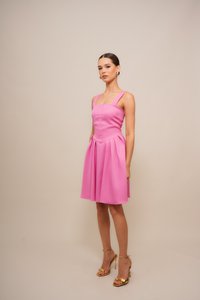 Rosa ärmelloses Kleid mit einem quadratischen Ausschnitt, gefaltetem Rock und Seitentaschen. Model trägt goldene Riemchen-High Heels und Ohrstecker.