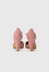 Escarpins en suède rose avec un bout pointu, présentant un design classique et un talon de hauteur moyenne. Sangle ajustable avec un petit détail de boucle.