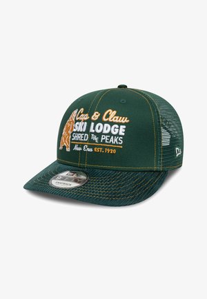 Căciulă verde cu un bec curbat. Prezintă un text brodat "Cabana de Schi Cap & Claw" și un grafic cu un urs. Spate din plasă, detalii cusute și închidere tip snapback.