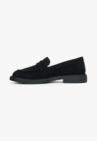 Zwarte suede instapschoenen met een ronde neus, platte rubberen zool en decoratieve band over de bovenkant. Gladde textuur met minimale stikseldetails.