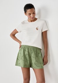 T-shirt en coton beige clair avec détails brodés ; associé à un short vert avec un motif texturé et une taille élastique.