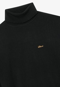 Maglione a collo alto di colore nero realizzato in tessuto lavorato a maglia. Presenta un colletto a coste e un piccolo logo dorato sul petto. Texture liscia.