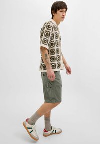 Kortærmet mønstret skjorte i creme og olivengrøn med firkantet design. Olivengrønne shorts med sidelommer og hvide sneakers med grønne detaljer.