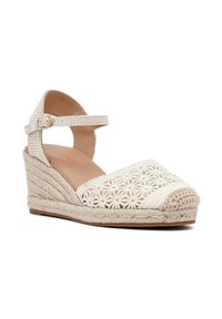 Espadrille de cuña con punta abierta, confeccionada en tejido trenzado color crema, con cortes florales y suela de yute trenzado. Correa para el tobillo con hebilla.