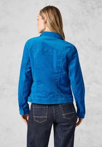 Blå bomullsdenimjacka med krage, knappade ärmslut och bakfickor. Har en strukturerad passform och en slät, hållbar textur.