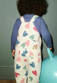 Beli kombinezon z barvnimi potiski src v rdeči, modri, zeleni in bež barvi, kombiniran z dolgimi rokavi modre majice. Otrok drži turkizni predmet.