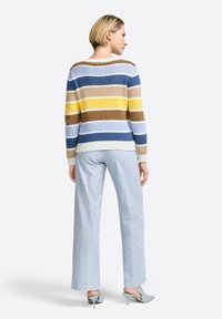 Striped knit sweater in beige, blue, and yellow; relaxed fit with ribbed neckline. Paired with light blue, wide-leg pinstripe pants and heels.