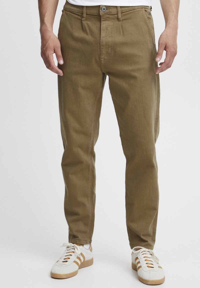Chino color khaki con una vestibilità dritta, dotato di passanti per cintura, chiusura frontale con bottone e tasche laterali. Abbinati a sneakers bianche.