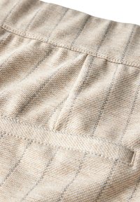 Beige tyg med tunna grå ränder, med en ficka och en texturerad yta. Designen är mjuk och vävd, vilket betonar en neutral färgpalett.