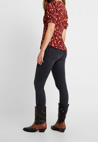 Blusa floral roja con mangas abullonadas combinada con vaqueros ajustados oscuros y botas vaqueras negras con acentos marrones y diseños de estrellas.