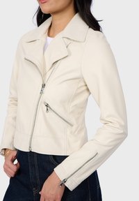 Crème leren motorjack met een uitgesneden kraag, asymmetrische rits aan de voorkant en twee ritszakken. Strak ontwerp met lange mouwen.