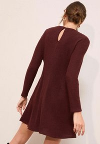 Bordo pletena haljina s teksturiranim dizajnom, dugim rukavima i otvorom u obliku ključanice na leđima. A-linija siluete s raširenim rubom.