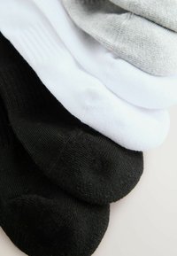 Fünf Paar Crew-Socken in Schwarz, Weiß und Grau. Das Material ist gestrickt, texturiert, mit gerippten Bändern an der Oberseite.