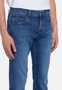 Jeans in denim blu con vestibilità slim, caratterizzati da uno stile classico a cinque tasche, leggeri effetti di sbiadimento e rivetti in rame sulle tasche.