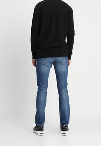 Niebieskie dżinsy o prostym kroju, z wyblakłym wykończeniem i dwiema tylnymi kieszeniami, połączone z czarnym swetrem i czarnymi trampkami.
