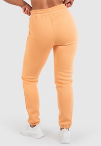  ferskenfarvede joggers lavet af blødt, strækbart stof; indsnittede manchetter; elastisk talje; minimal syning; parret med hvide sneakers.