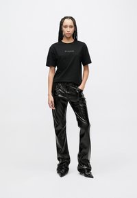 Μαύρο βαμβακερό T-shirt με λογότυπο "PINKO" σε χρυσό, σε συνδυασμό με γυαλιστερό μαύρο παντελόνι φαρδιάς γραμμής από ψεύτικο δέρμα. Η υφή του υφάσματος είναι γυαλιστερή.