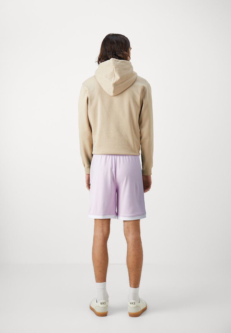 Un hoodie beige avec une capuche à cordon, associé à un short violet clair avec une bordure blanche. Des baskets blanches avec une semelle marron clair.