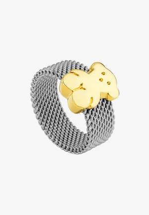 Anillo de malla plateada con un charm en forma de oso dorado con un acabado suave y pequeñas perforaciones para los detalles faciales.