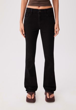 Jean en denim noir évasé avec cinq poches, une fermeture à bouton à l'avant et des coutures ton sur ton, présentant une texture lisse et un design structuré.
