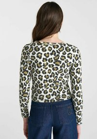 Geribbelde lange mouw top met een witte achtergrond en zwarte en olijfgroene luipaardprint. Heeft een ronde halslijn en een aansluitende silhouet.