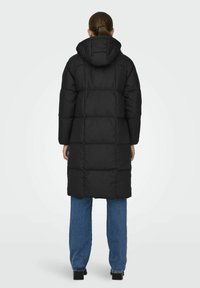 Svart boblejakke med hette, med quiltet design og lange ermer. Kombinert med blå denimbukser. Enkelt, funksjonelt stil.